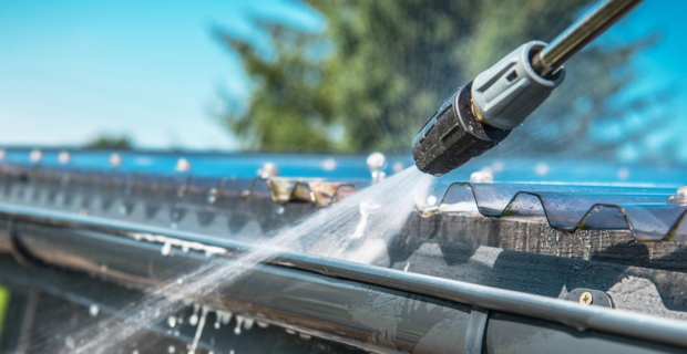 A homeowner cleans out their gutters with a power washer. 