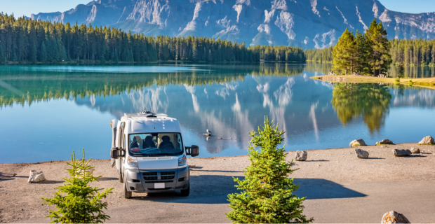 An RV is parked by a lake in an Alberta national park with the rocky mountains in the background. 