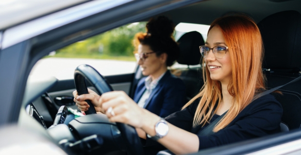 A young woman with red hair driving a vehicle during a drivers’ education class with a female instructor.
