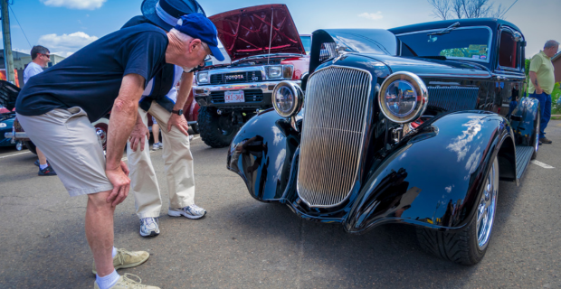 An older man getting a closer look at a 1933 Plymouth coupe parked in a downtown area.