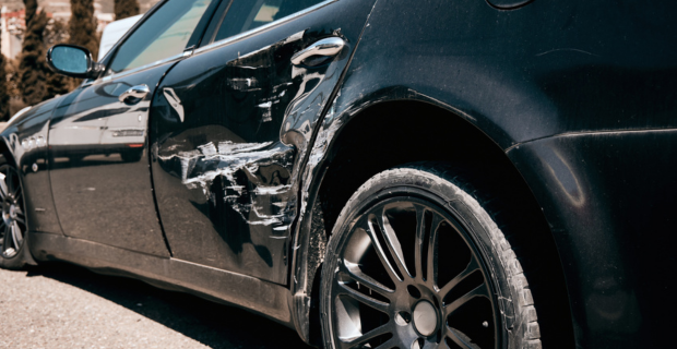 Close up of a black car with structural damage on the side of it. 