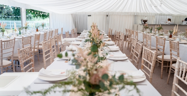 Wedding reception in a white marquee with flowers and table decorations.