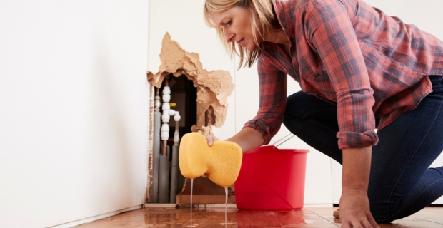 Worried woman mopping up water from a burst pipe with sponge