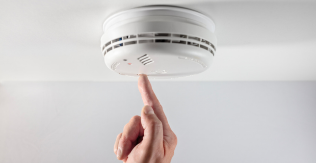 Person pushing the button on a home smoke alarm.