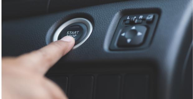 Close-up of a finger hovering over the keyless start button on a car dashboard.