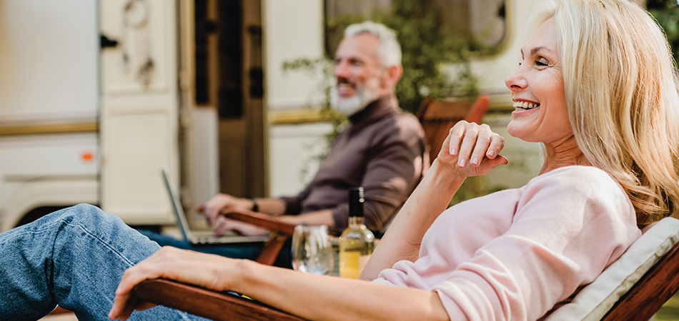 Mature couple relaxing on deck chairs near their mobile home with a bottle of wine