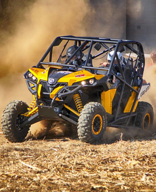 Two riders in an ATV with a cage ride through a dry field.