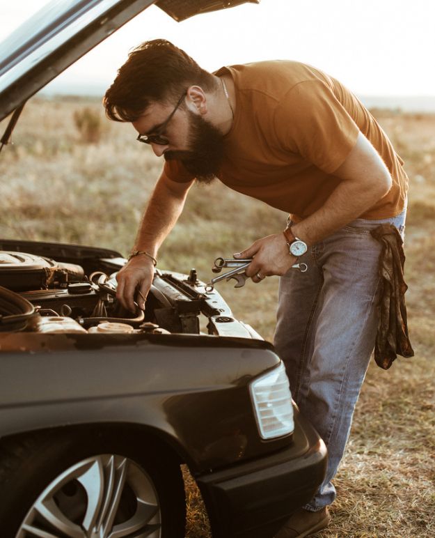 A bearded man in his 20s working on his car.