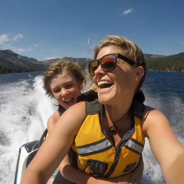 A parent and their child, wearing life jackets, laughing and smiling as they ride on their Sea-Doo.