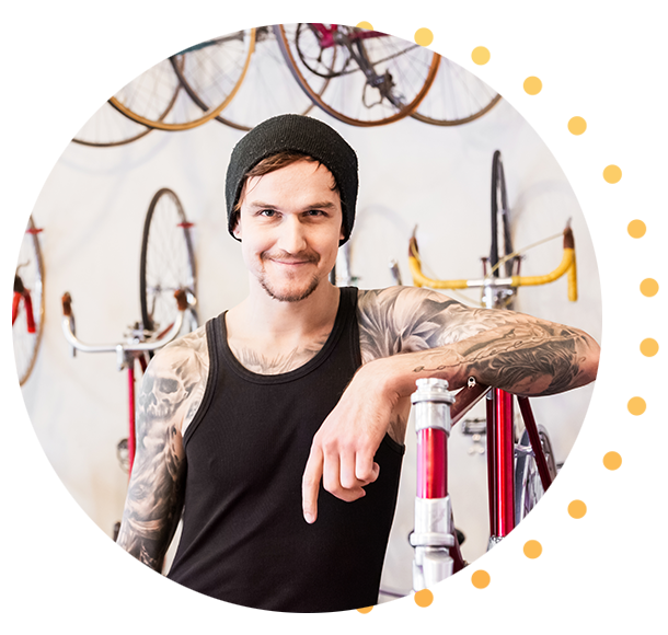 A tattooed man in his early 30s stands at the counter of his bicycle shop.