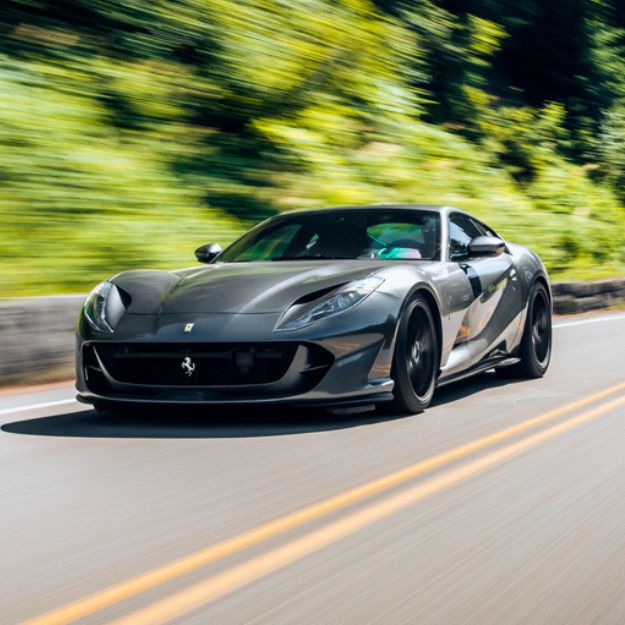 A charcoal-black modern collector car driving fast on a scenic highway.