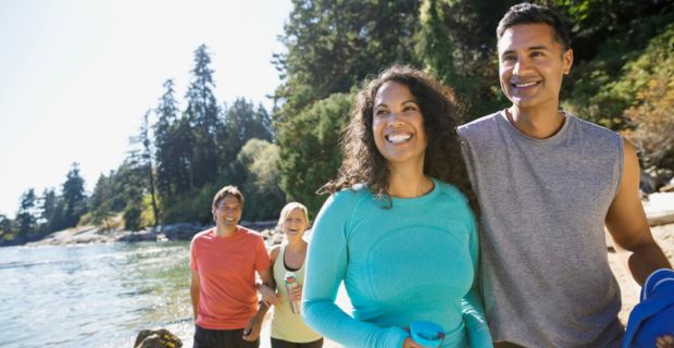 Two couples are walking arm in arm along the edge of a beautiful river on a sunny day in Alberta.