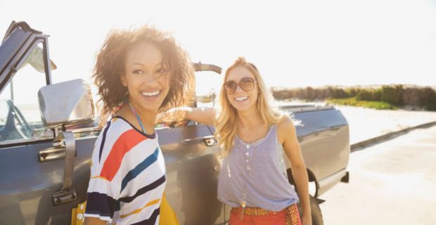 Two smiling women standing next to a convertible car