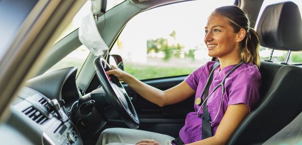 A doctor smiles from the driver's seat in her car.