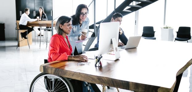 A wheelchair user working alongside one of her colleagues in an open concept office. 