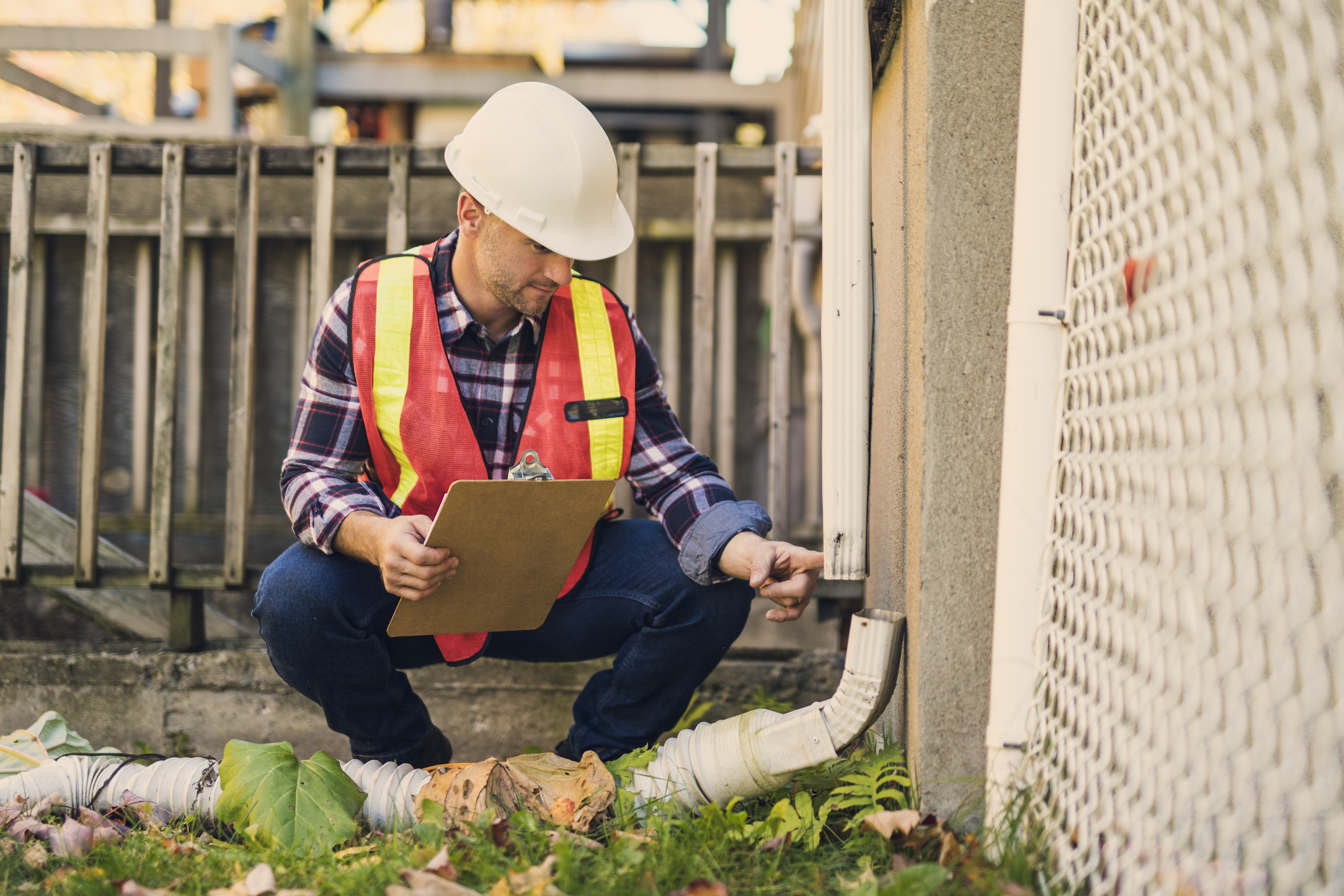 Man in hard hat and vest checking water spout against building outdoors