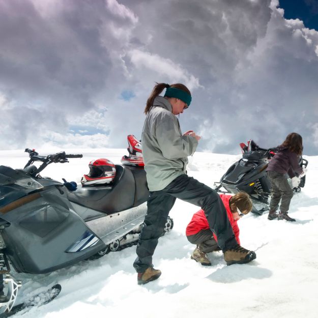 A group of adults and children stopped for a break beside their snowmobiles on a winter day.