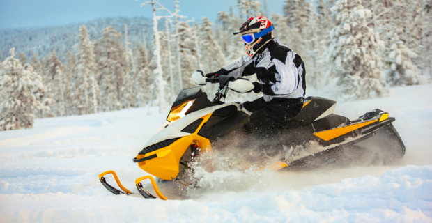 Snowmobile rider seen riding through snow on a snowy landscape surrounded by winter forest.