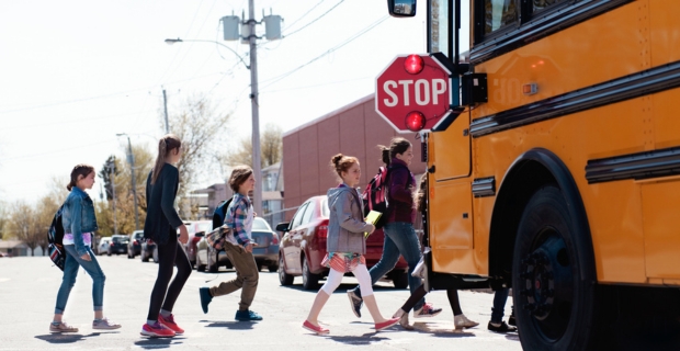 Students crossing safely in front of a school bus. The bus’s stop sign is extended and its lights are flashing.