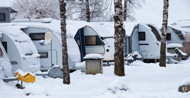 A row of RVs covered in snow during the winter.