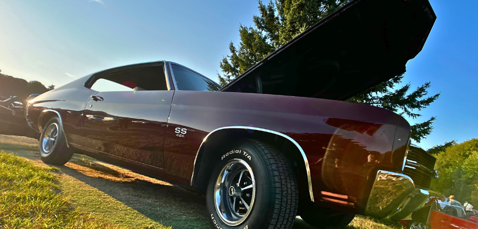 A classic dark red Chevrolet Chevelle SS muscle car parked on grass at an outdoor car show, photographed.