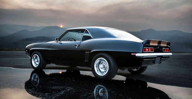 A black Chevrolet Camaro is parked on a gravel road by mountains.