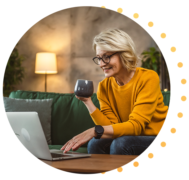 A woman holding a mug and looking at a laptop