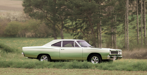 A green Plymouth Road Runner parked in a grass field by trees.