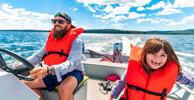 A father and his daughter are on their boat wearing life jackets, practicing safe boating.