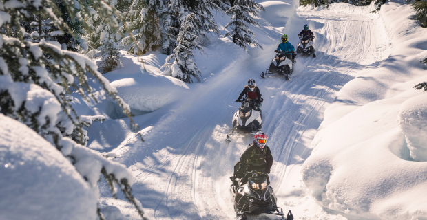 A group of people snowmobiling on a trail in the winter.