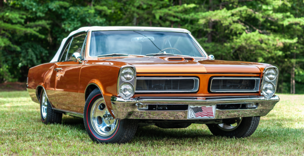 An orange Pontiac GTO parked in a grass field.