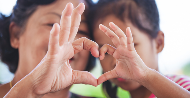 An adult and child joining their hands into a heart shape.