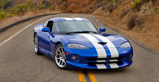 A blue Dodge Viper GTS with white racing stripes is parked in the middle of a road in the hills.