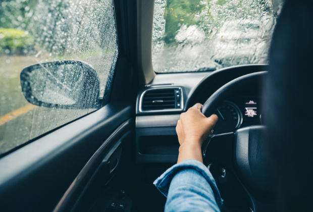 A photo of someone driving a car in the rain, taken from the seat behind the driver. Their right hand gripping the steering wheel is all you can see of the driver. 