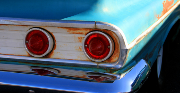 Back view of a classic car with rust around the taillights and on the body as well. 